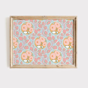 May include: A framed print featuring a repeating floral pattern. The design includes circular motifs with pink flowers and orange centers, set against a light blue background. Pink leaf-like shapes and a gold-colored frame complete the artwork.