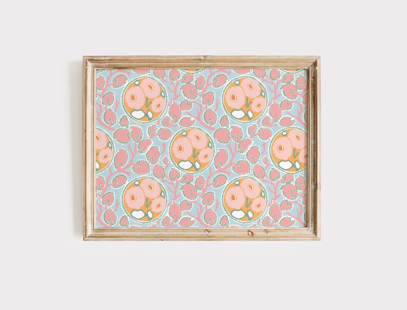 May include: A framed print featuring a repeating floral pattern. The design includes circular motifs with pink flowers and orange centers, set against a light blue background. Pink leaf-like shapes and a gold-colored frame complete the artwork.