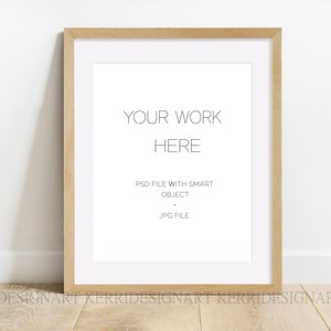 Puede incluir: Un marco de madera clara con un paspart&uacute; blanco y un fondo blanco. El texto "YOUR WORK HERE" est&aacute; impreso en el centro del marco. Debajo del texto se encuentra "PSD FILE WITH SMART OBJECT" y "JPG FILE".