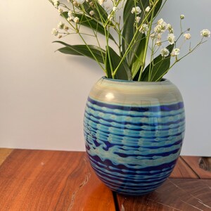 May include: A blue and white glass vase with a wavy pattern, filled with white flowers.