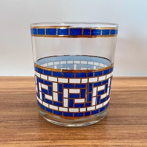 May include: A clear glass tumbler with a decorative mosaic pattern. The design features blue and white geometric shapes with gold trim. The glass is suitable for serving beverages.