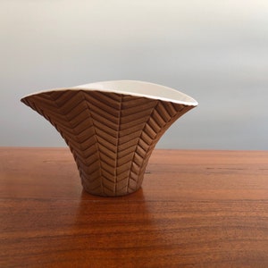 May include: A brown ceramic vase with a white interior and a chevron pattern. The vase is shaped like a wide, shallow bowl with a flared rim.