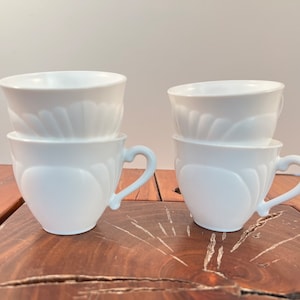 May include: Four white ceramic cups with a decorative embossed design. The cups are stacked in pairs.