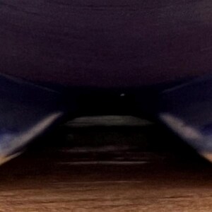 May include: A dark blue ceramic bowl with three rounded feet. The feet have a lighter blue gradient with a white edge. The bowl sits on a light brown wooden surface.