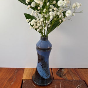 May include: A small blue and black ceramic vase with white flowers. The vase has a black and white design with the word "Dream" written on it.