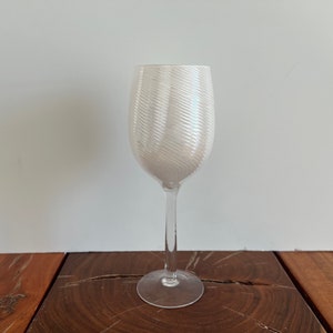 May include: A white wine glass with a swirling, textured design. The glass has a clear stem and a round base.