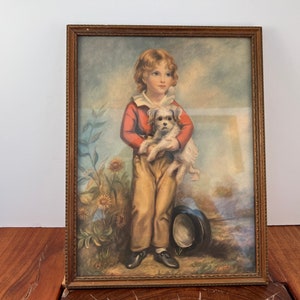 May include: Vintage framed print of a young person holding a small white dog. The person is wearing a red jacket, tan pants, and black shoes. The background features a garden scene with sunflowers and a hat.