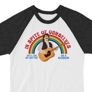 Puede incluir: Una camiseta de béisbol raglán blanca y carbón con un gráfico de un hombre tocando la guitarra frente a un arcoíris. El texto dice "IN SPITE OF OURSELVES" y "WE'LL END UP SITTIN' ON A RAINBOW".