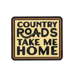 Op de afbeelding: Een gele en zwarte sticker met de tekst "Country Roads Take Me Home" in een vet, zwart lettertype. De tekst "Roads" heeft een gestileerd wegontwerp erboven.