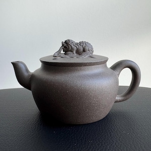 以下が含まれることがあります： 丸みを帯びたボディ、湾曲したハンドル、注ぎ口を備えた茶色のセラミックティーポット。蓋には、神話上の生き物の詳細な彫刻が施されています。ティーポットは紅茶を淹れるために設計されており、クラシックでエレガントな外観をしています。