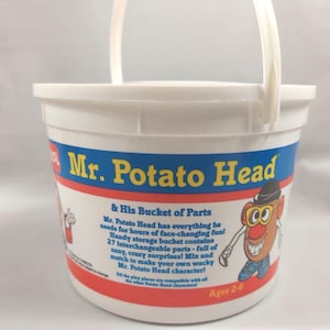 May include: A white plastic storage bucket for Mr. Potato Head & His Bucket of Parts. The label features yellow text, a red stripe, and an illustration of the character. The text describes 27 interchangeable parts for ages 2-6.