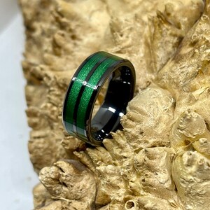 May include: A black tungsten carbide ring with a green wood inlay. The ring has two parallel lines of green wood inlay.