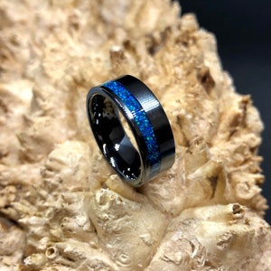 May include: A black tungsten carbide ring with a blue opal inlay. The ring is polished and has a beveled edge.