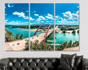 May include: A panoramic view of a red bridge over a body of water. The bridge is surrounded by lush green trees and a blue sky with white clouds. Cars are driving across the bridge.