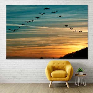 May include: A flock of geese flying in a V formation against a colourful sunset sky. The geese are silhouetted against the orange, yellow, and blue hues of the sky.