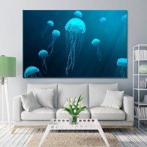 May include: A wall art print featuring a group of glowing blue jellyfish swimming in a dark blue ocean. The jellyfish are translucent and have long, flowing tentacles.