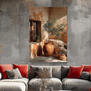 Op de afbeelding: Een canvas print met een zonnige hoek met een terracotta pot met een kleine olijfboom. De scène omvat een raam, stenen accenten en een neutraal kleurenpalet. Het kunstwerk wordt weergegeven boven een grijze bank met rode en grijze sierkussens.