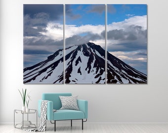 May include: A snowy mountain peak with a dark, rocky summit against a blue sky with white clouds.