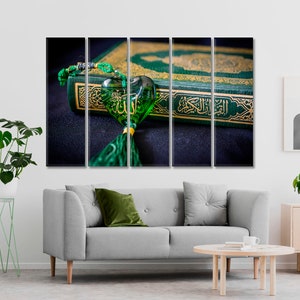 May include: A green and gold Quran with a green heart-shaped charm with Arabic calligraphy. The charm is hanging from a green tassel.