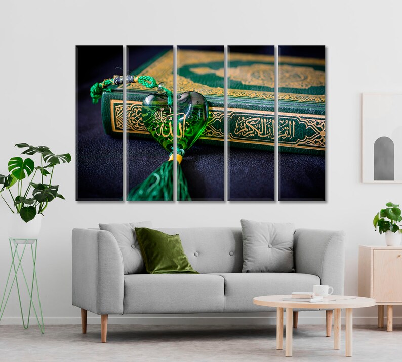 May include: A green and gold Quran with a green heart-shaped charm with Arabic calligraphy. The charm is hanging from a green tassel.