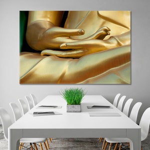 May include: Close-up of a golden Buddha statue's hands in a meditation pose. The hands are clasped together, with the fingers intertwined. The statue is made of a smooth, shiny material, and the light reflects off of the surface.