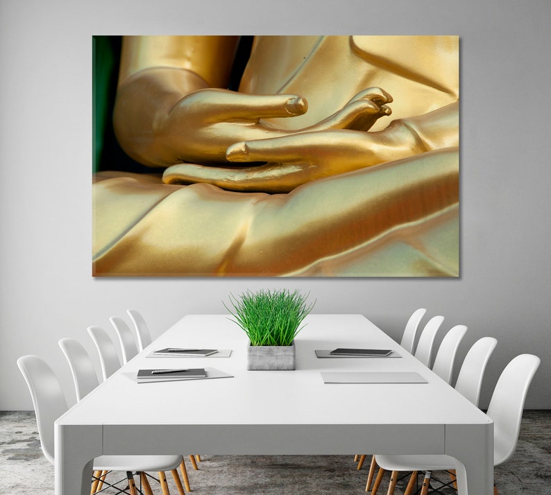 May include: Close-up of a golden Buddha statue's hands in a meditation pose. The hands are clasped together, with the fingers intertwined. The statue is made of a smooth, shiny material, and the light reflects off of the surface.