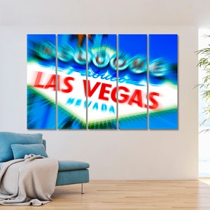 May include: A multi-panel canvas print featuring a close-up of the iconic "Welcome to Fabulous Las Vegas" sign with a blurred, motion-effect background. The sign is illuminated with bright red and white lettering against a blue sky.