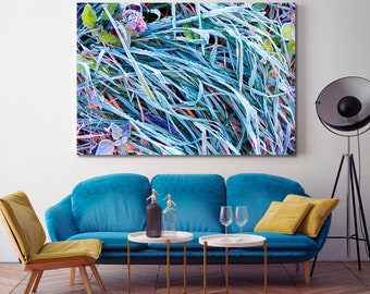 May include: A close-up photograph of a canvas print featuring a frosty, blue-green grass field. The print is hanging on a white wall above a blue velvet sofa with two gold side tables and two wine glasses.