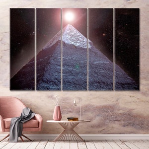 May include: A multi-panel canvas print depicting a pyramid under a starry night sky with a bright light above. The pyramid is a dark blue color, and the sky is a deep purple. The print is displayed above a pink chair and a white table.