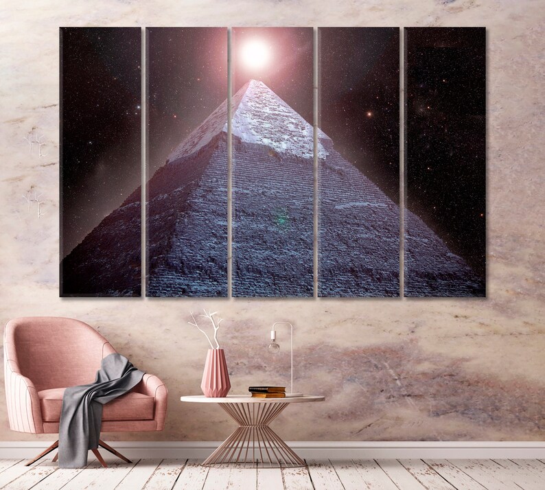 May include: A multi-panel canvas print depicting a pyramid under a starry night sky with a bright light above. The pyramid is a dark blue color, and the sky is a deep purple. The print is displayed above a pink chair and a white table.