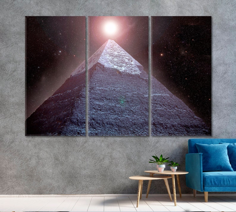 May include: A three-panel canvas print depicting a pyramid under a bright light in a starry night sky. The pyramid is constructed of dark gray stone blocks. The artwork is displayed above a blue sofa and a small wooden table.