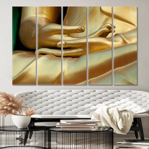 May include: Close-up of a golden Buddha statue's hands in a meditative pose. The statue is made of smooth, polished gold and the hands are folded together in a gesture of peace and tranquility.
