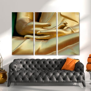 May include: A close-up of a golden Buddha statue's hands, with the fingers intertwined in a meditative pose. The statue is made of a smooth, shiny material, and the light reflects off its surface.