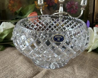May include: A clear, faceted crystal bowl with a round shape and a decorative base. The bowl has a diamond pattern and a blue and white "Bohemia" sticker. A silver candelabra is in the background.
