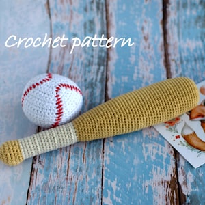 May include: Crocheted baseball and bat toy set. The baseball is white with red stitching. The bat is beige with a brown handle. The toys are on a blue wooden background.