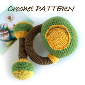 May include: Crochet pattern for a green and yellow rattle toy. The rattle has a brown handle and two round ends with yellow and green stripes.