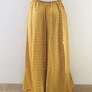 Puede incluir: Pantalones palazzo de color amarillo mostaza con estampado de cuadros blancos. Los pantalones tienen una pierna ancha y un ajuste holgado.