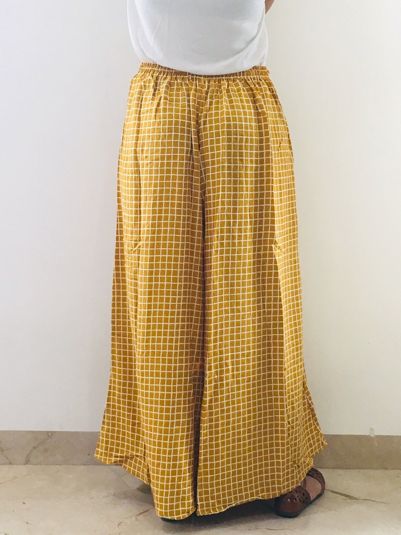 Puede incluir: Pantalones palazzo de color amarillo mostaza con estampado de cuadros blancos. Los pantalones tienen una pierna ancha y un ajuste holgado.