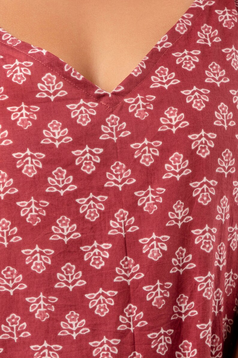 K&ouml;nnte beinhalten: Nahaufnahme eines roten Stoffes mit einem wei&szlig;en Blumenmuster. Der Stoff hat einen V-Ausschnitt und ist aus einem weichen, leichten Material gefertigt.