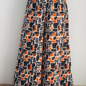 Puede incluir: Pantalones palazzo de pierna ancha con un patr&oacute;n geom&eacute;trico en tonos naranja, negro y blanco.