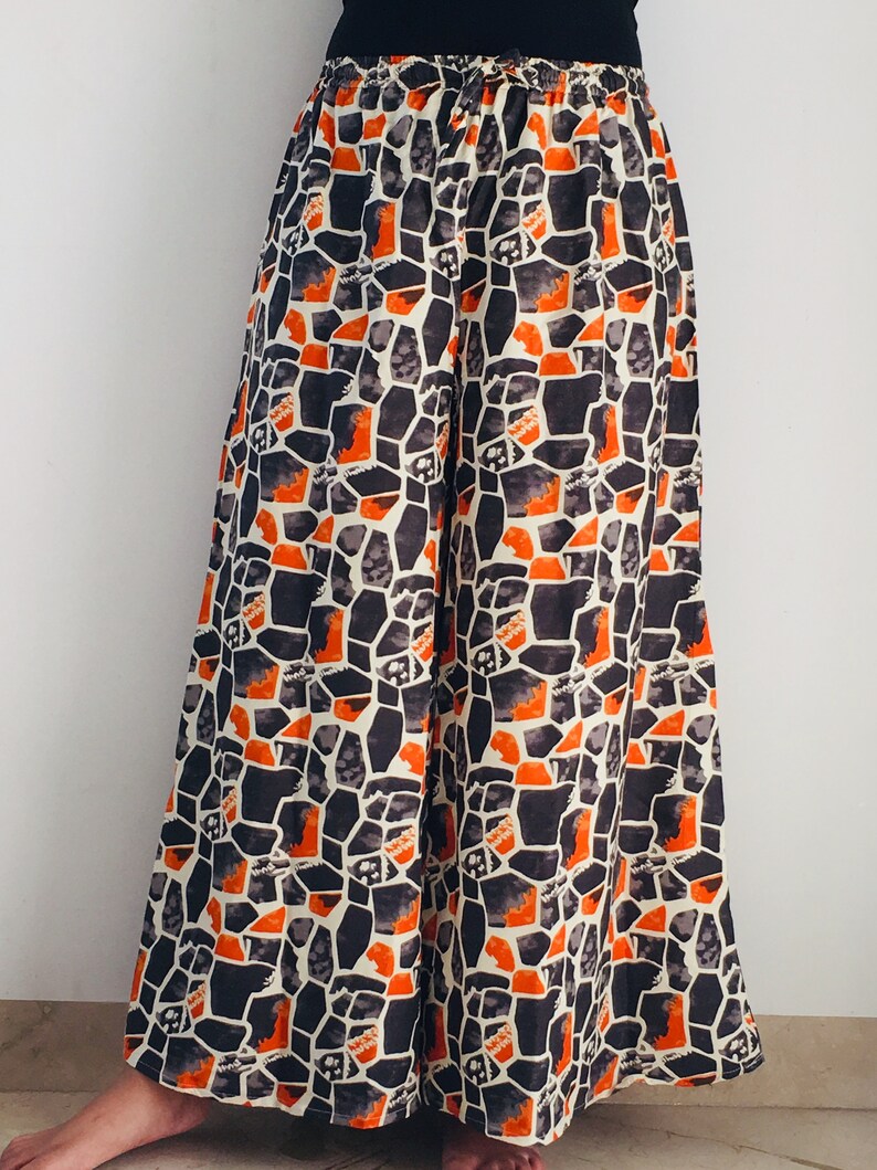 Puede incluir: Pantalones palazzo de pierna ancha con un patr&oacute;n geom&eacute;trico en tonos naranja, negro y blanco.