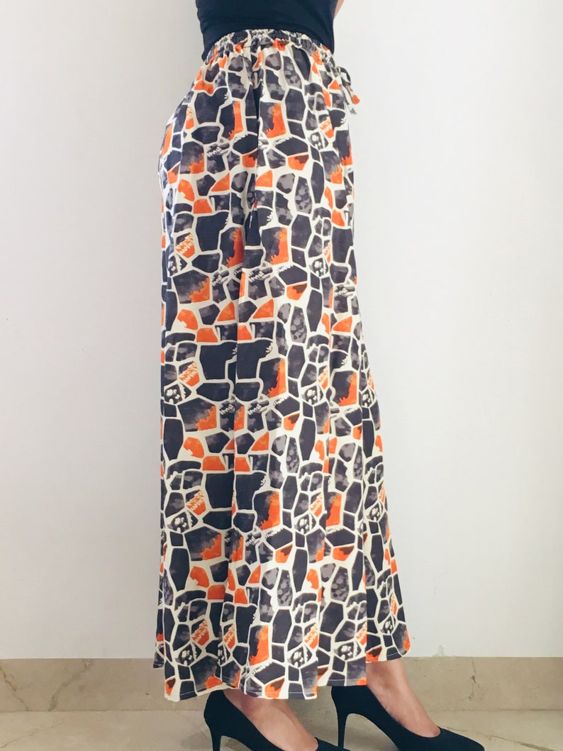 Puede incluir: Pantalones de pierna ancha con un patr&oacute;n geom&eacute;trico en tonos naranja, negro y blanco.