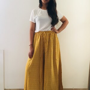 Puede incluir: Una mujer con una camiseta blanca y pantalones palazzo a cuadros amarillos y blancos.