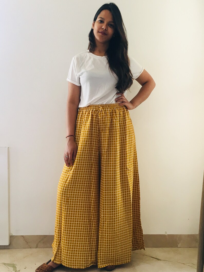 Puede incluir: Una mujer con una camiseta blanca y pantalones palazzo a cuadros amarillos y blancos.