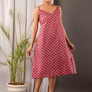 K&ouml;nnte beinhalten: Eine Frau tr&auml;gt ein maronfarbenes, &auml;rmelloses Midikleid mit wei&szlig;em Blumenmuster. Das Kleid hat einen V-Ausschnitt und eine lockere Passform. Sie tr&auml;gt transparente Sandalen mit Absatz.
