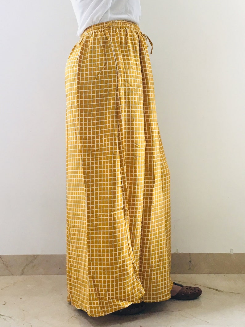 Puede incluir: Pantalones palazzo de color amarillo mostaza con estampado de cuadros blancos. Los pantalones tienen una cintura con cord&oacute;n y una pierna ancha.