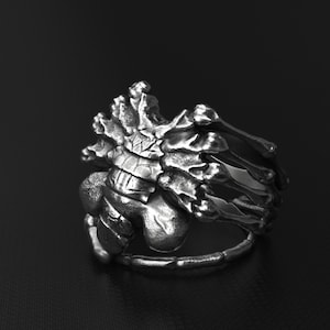 Könnte beinhalten: Ein silberner Ring mit einem Skelett-Design. Der Ring besteht aus einer Reihe von miteinander verbundenen Knochen, die ein komplexes und filigranes Muster bilden.