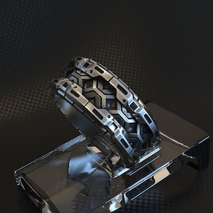 Puede incluir: Un anillo de plata con un diseño geométrico. El anillo está hecho de metal y tiene una superficie texturizada.