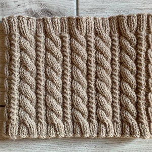 May include: A beige knitted cowl with a cable knit pattern.