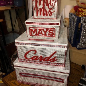 Puede incluir: Un conjunto de cajas decorativas, ideal para una boda o evento especial. Las cajas blancas est&aacute;n cubiertas de pedrer&iacute;a plateada, con detalles rojos y letras que dicen "Mr & Mrs", "Mays" y "Cards".